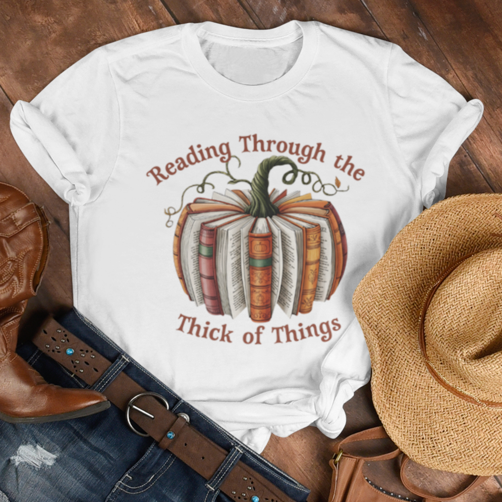 White t-shirt with pumpkin design and text, paired with cowboy boots, denim shorts, a straw hat, and brown purse on wooden surface. Text is Reading Through the Thick of Things.